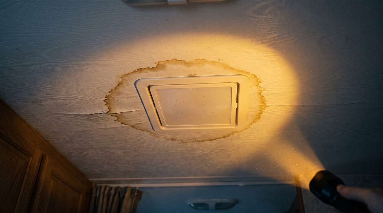 water stain spreading across an interior RV ceiling panel below a roof vent