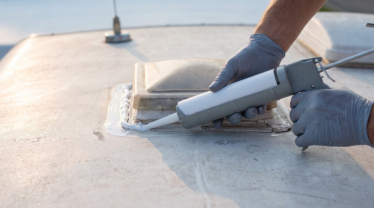 hands applying fresh white lap sealant around a plastic roof vent base