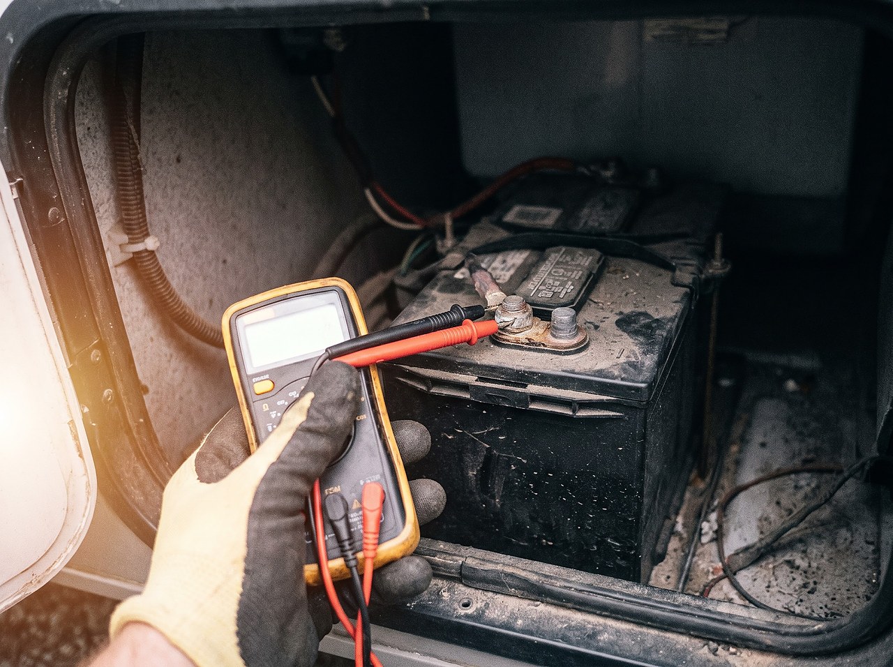 hand holding multimeter probes against RV battery terminals to check voltage under load